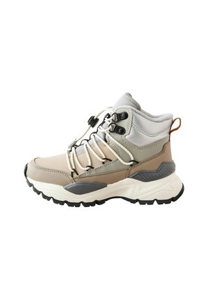 Beige und graue Wanderschuhe mit dickem Profil, gepolstertem Knöchelschutz und weißen Schnürsenkeln, die mit einem schwarzen Clip befestigt sind, isoliert auf weißem Hintergrund.