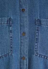 Jeansskjorta i en livlig blå färg, mörka metallknappar och dubbla bröstfickor med synlig sömnadstekstur.