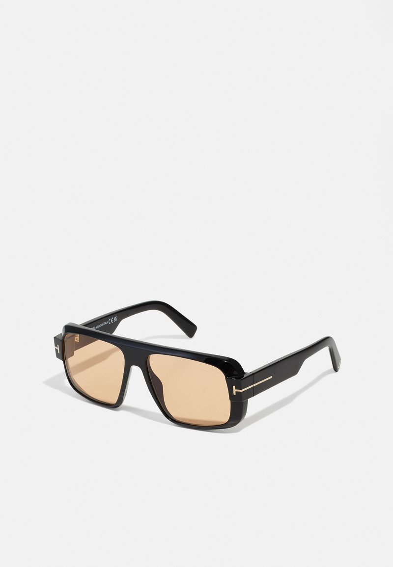 Occhiali da sole neri con forma rettangolare, lenti colorate di marrone e dettagli dorati sulla montatura. Finitura lucida con tempie spesse.