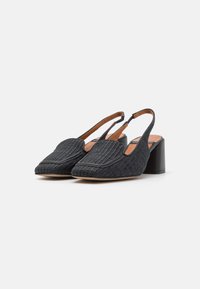 Chaussures à talons blocs à bride arrière noires en tissu texturé, avec un bout pointu et une semelle intérieure contrastante beige. Présente un panneau décoratif à l'avant.