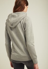Felpa grigia con cappuccio, realizzata in materiale morbido, caratterizzata da un design semplice e polsini e orli a coste. Senza loghi o motivi visibili.