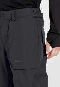 Pantalones de snowboard negros con un acabado mate y suave. Incluyen cinturón, bolsillos y un sutil logo de la marca en el lado.