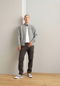 Gray textured bomber jacket with a zip front, white t-shirt underneath, dark cargo pants, and gray sneakers. Simplistic and functional design.