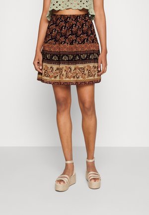 Zwart en bruin patroon rok met een uitlopende snit, voorzien van bloem- en paisleymotieven. Gecombineerd met lichtgekleurde espadrilles.