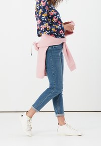 Svetry s námořnickým květinovým vzorem, světle růžový pletený svetr uvázaný v pase, modré slim-fit džíny a bílé šněrovací tenisky, vystavené na bílém pozadí.