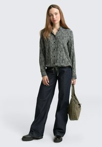 Schwarz-weißer gestreifter Knopf-up Hemd, lockere Passform, kombiniert mit dunkelblauen weiten Jeans. Das Modell hält eine grüne Handtasche mit Texturdetails.