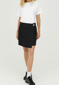 Musta kietaisuhame, jossa etutasku ja koristeellinen nappi. Yhdistetty yksinkertaiseen valkoiseen t-paitaan ja mustiin tennareihin, luoden rento ilmeen.