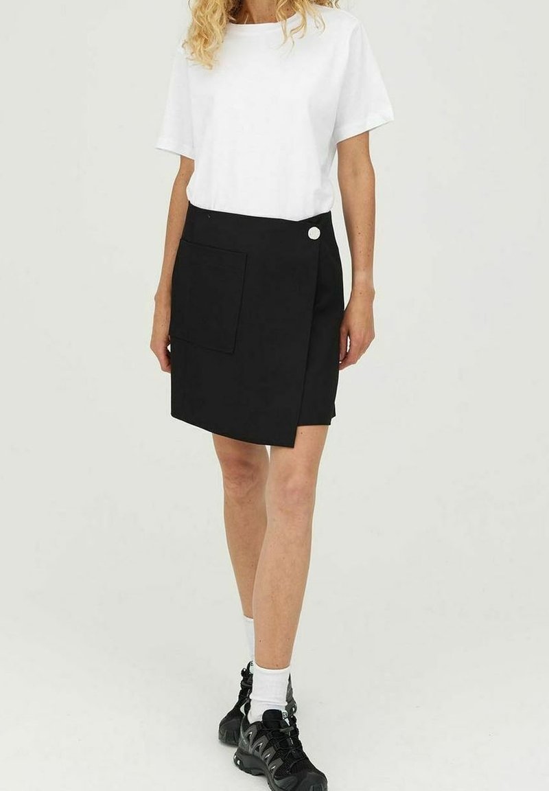 Musta kietaisuhame, jossa etutasku ja koristeellinen nappi. Yhdistetty yksinkertaiseen valkoiseen t-paitaan ja mustiin tennareihin, luoden rento ilmeen.