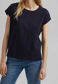 Mørkeblå kortærmet bluse med struktureret stof, der har en rund hals og et subtilt mønster. Sammen med blå jeans.