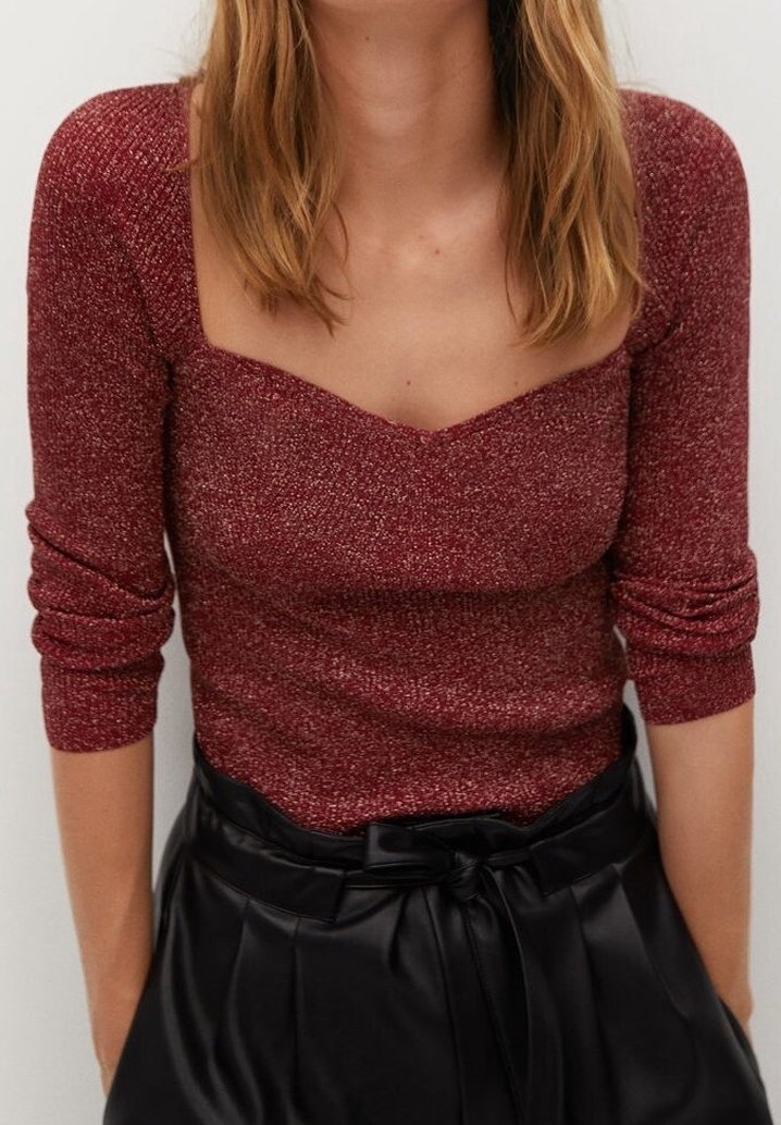 Femme portant un haut en maille ajusté à manches longues couleur bordeaux avec un décolleté en cœur et un pantalon en cuir noir taille haute style paperbag avec ceinture nouée.