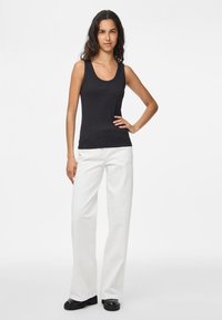 Černý žebrovaný top na ramínka s kulatým výstřihem, v kombinaci s bílými širokými kalhotami, doplněný lesklými černými botami. Jednoduchý a přiléhavý design.