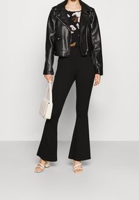 Svart läderjacka, blommig topp, utsvängda svarta byxor, vita blockklack sandaler och en liten creamfärgad handväska med ett kviltat mönster.