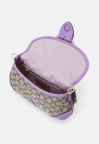 Svævet håndtaske med en brun monogram canvas overflade, lilla læderkanter og en rummelig indvendig med lilla stofforet, der har lynlås- og slip-lommer.