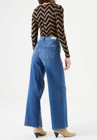 Denim wide-leg jeans in medium blue with a high waist, featuring back pockets and a slightly cropped length, paired with a patterned top.