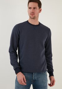 Jūras flotes crewneck džemperis ar ribotām piedurknēm un apakšmalu, ar smalku teksturētu rakstu. Uzvilkts virs gaiši zilām džinsām.