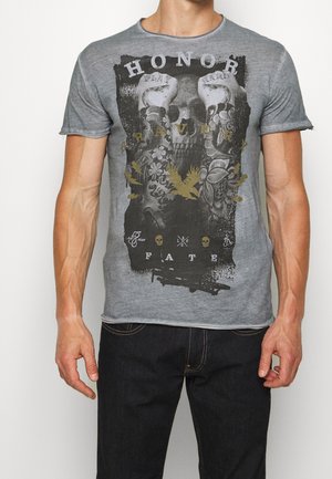 Grå t-shirt med korte ærmer, der har et grafisk print af kranier, blomster og tekst i sort og guld, med en slidt tekstur og skarp halsudskæring.