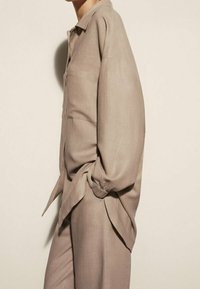 Langarm, beige shirt gemaakt van zachte stof met een ontspannen pasvorm, voorzien van een kraag en een borstzak, gestyled met licht opgerolde mouwen.