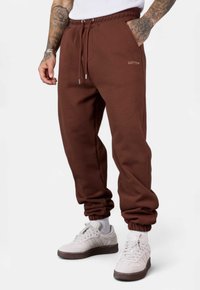 Braune Baumwoll-Jogginghose mit elastischem Bund, seitlichen Taschen und gerippten Bündchen; verfügt über ein minimalistisches Logo auf der Vorderseite.