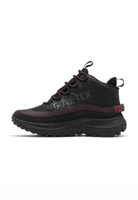 Chaussure de randonnée montante noire avec couture rouge, étiquette Gore-Tex, semelle robuste et languettes en tissu sur la languette et le talon.