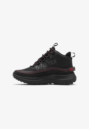 Mustat korkeavartiset vaelluskengät punaisilla ompeleilla, Gore-Tex -merkki, kestävä pohja sekä kangaspullot vetoketjussa ja kantapäässä.