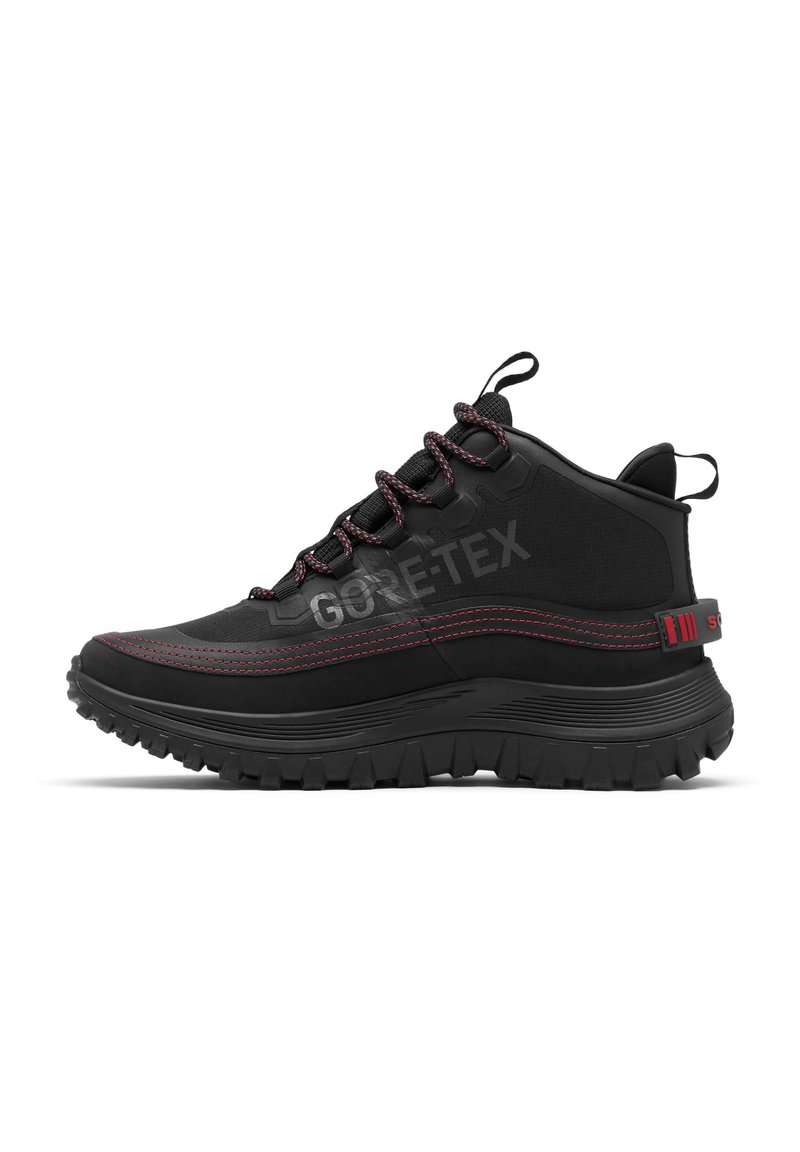 Chaussure de randonnée montante noire avec couture rouge, étiquette Gore-Tex, semelle robuste et languettes en tissu sur la languette et le talon.