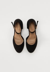 Svarta mockaskor med klack och öppen tå-design, sidoband med spänne och en subtil beige innersula. Slät textur och böljande silhuett.