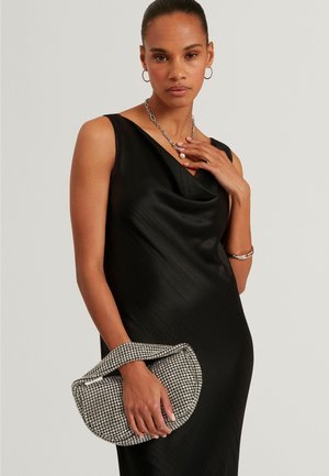 Abito nero con collo alla cieca e trama plissettata. La modella tiene in mano una borsa argentata impreziosita da strass con tracolla. Accessori in argento.