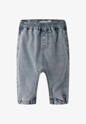 Vaqueros para niño pequeño con cintura elástica de color azul claro, bajos remangados y un pequeño parche de oso cerca del tobillo izquierdo.