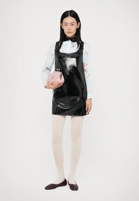 Μαύρο πατέντ δέρμα φόρεμα με τετραγωνισμένο ντεκολτέ, φορεμένο πάνω από μια ανοιχτό μπλε λουλουδένια μπλούζα. Το μοντέλο κρατάει μια ροζ τσάντα φάκελο, φοράει λευκές καλσόν και σκούρα παπούτσια.