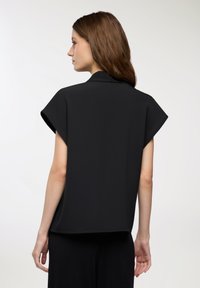 Blusa nera a maniche corte con una vestibilità rilassata, dotata di colletto e linee pulite, realizzata in tessuto liscio. Il retro è semplice, senza decorazioni.