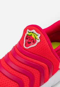 Jasnoczerwony sneakers z fakturowaną cholewką, żłobieniami i naszywką z grafiką truskawki na języku. Biała podeszwa i zielone wykończenie.