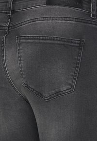 Jeans skinny cinza escuro feitos de denim, apresentando um design clássico de cinco bolsos com um bolso traseiro distinto e detalhes de costura visíveis.