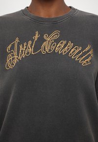 Γκρίζα μπλούζα με στρογγυλή λαιμόκοψη, με το "Just Cavalli" διακοσμημένο με χρυσές ραβδώσεις πέτρας στο στήθος. Μαλακό ύφασμα.