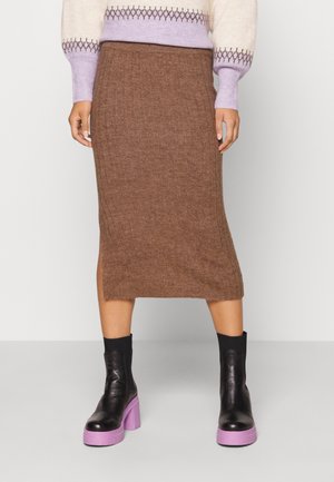 Femme portant une jupe midi côtelée marron, des bottines noires avec des semelles épaisses lavande, et un pull crème avec un motif lavande.