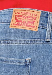 Pantalones vaqueros de mezclilla azul con un parche de cuero marrón que muestra "Levi Strauss & Co." y dos gráficos de caballos. Presenta costura estándar en los bolsillos traseros.