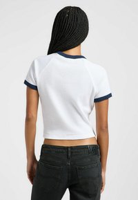 Hvid cropped t-shirt med marineblå accenter og ribbet tekstur; parret med sorte jeans med lommer og et label på taljen.