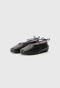 Pantofi din piele neagră cu o formă rotunjită, având un detaliu sub formă de fundă pe lateral și o textură netedă, concepuți pentru confort cu o talpă plată.