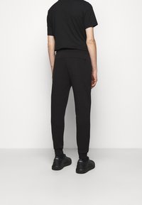 Schwarze sportliche Jogginghosen mit einer figurbetonten Passform, elastischem Bund und gerippten Knöcheln. Kombiniert mit schwarzen Freizeitschuhen.