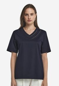 Marinblå t-shirt med kort ärm och V-halsdesign som har lager av trimdetaljer. Tyget ser slätt och lättviktigt ut.