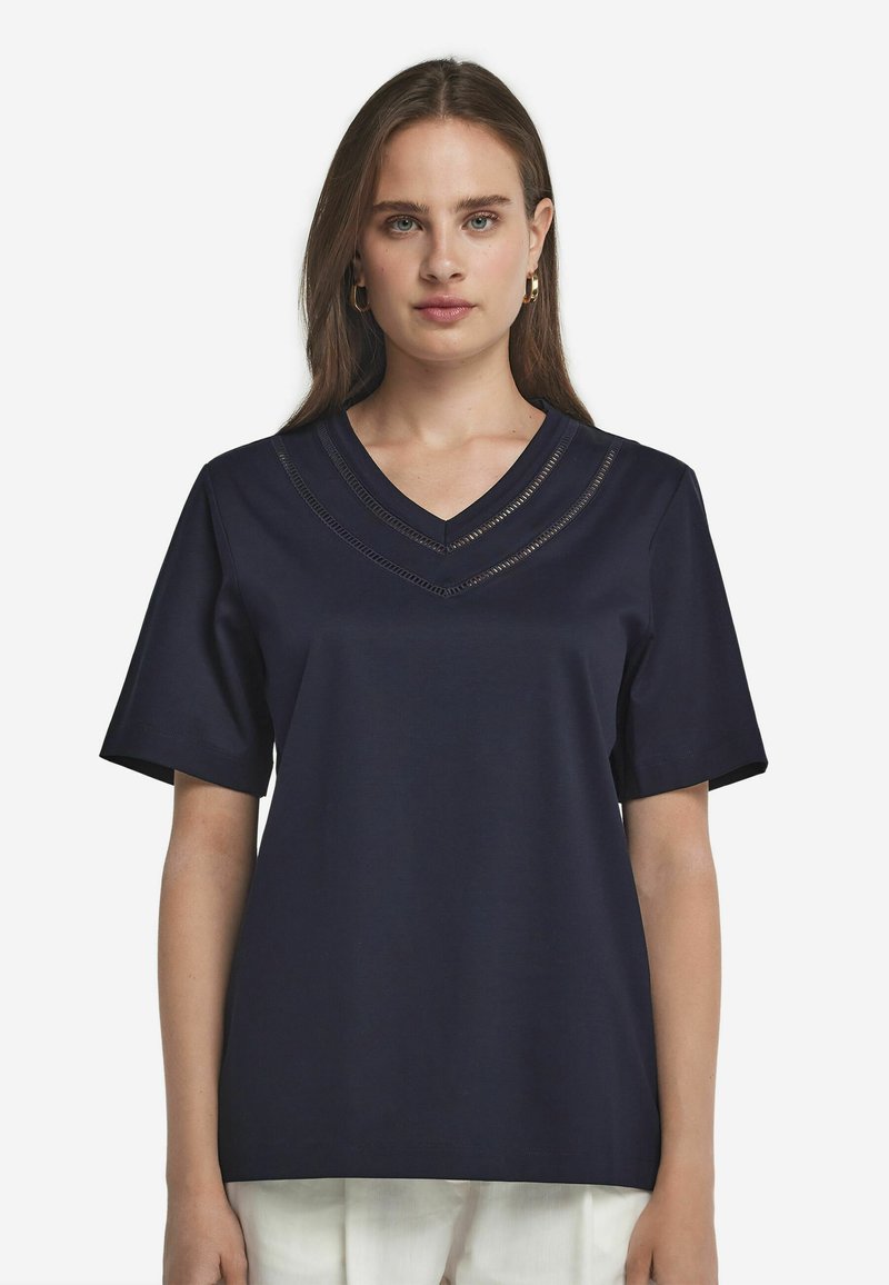 Marinblå t-shirt med kort ärm och V-halsdesign som har lager av trimdetaljer. Tyget ser slätt och lättviktigt ut.