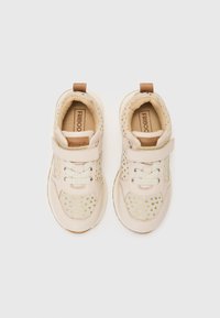 Baskets beige clair avec des accents dorés, dotées d'un col rembourré, d'une sangle à boucle et d'une semelle en caoutchouc contrastante.