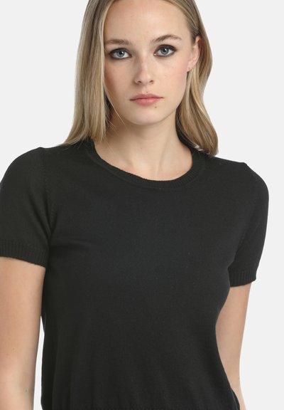 Juodas trumpas rankovėmis mezginys su apvalia iškirpte. Lygus tekstūra su raukšiniais ant rankovių ir krašto. Paprastas, prigludęs dizainas.