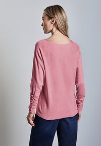 Maglietta rosa a maniche lunghe con una vestibilità comoda, caratterizzata da un collo largo e maniche arricciate; abbinata a pantaloni in denim scuro.