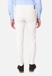 Pantaloni bianchi slim-fit con una texture liscia, dotati di due tasche posteriori e un accento in pelle marrone in vita. Indossati con scarpe marroni scure.