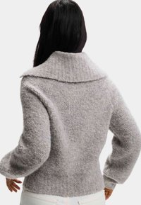 Szary, teksturowany sweter z szerokim kołnierzem i prążkowanymi detalami. Rękawy są lekko bufiaste, tworząc przytulny kształt.