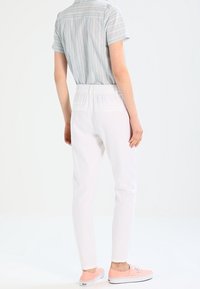 Pantalons blancs fuselés avec taille élastique, offrant une texture lisse. Assortis à une chemise à manches courtes rayée bleu clair et des baskets roses.