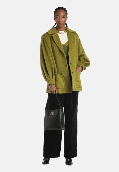 Olijfgroene oversized wollen jack van een wolmix met grote knopen en twee voorzakken, gecombineerd met zwarte corduroy broek en een zwarte tote bag.