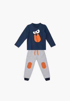 Chemise à manches longues navy avec un graphique de visage de chien blanc et orange ; pantalon gris avec des patches de genoux à motif de grille orange et des poignets navy.