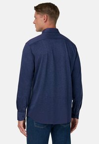 Mörkblå långärmad skjorta med knäppkrage, texturerat tyg och rundad nederkant. Har knappmanschetter och en skräddarsydd passform.