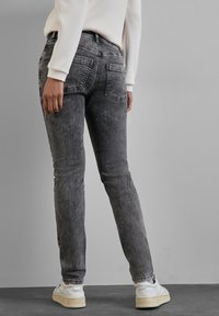 Jean en denim gris foncé avec une coupe slim, comportant deux poches arrière et un léger effet de décoloration. Associés à des baskets blanches.